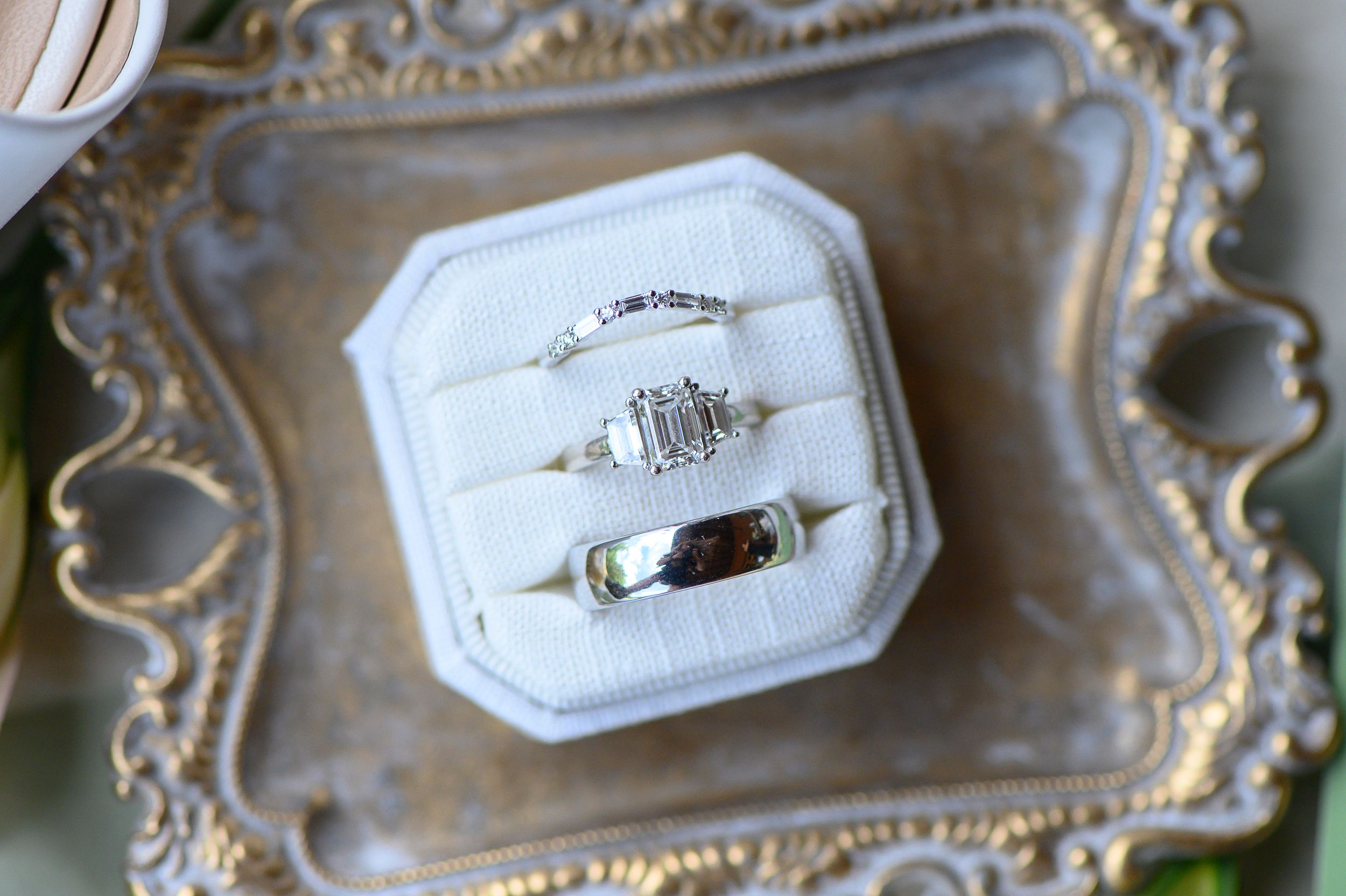 Three elegant wedding rings displayed in a white velvet ring box on a vintage silver tray.