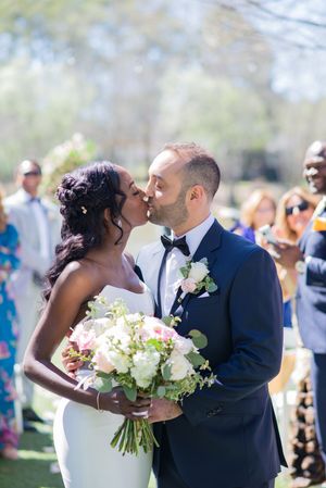 A romantic outdoor wedding ceremony with a couple kissing while holding a beautiful white and pink floral bouquet. rays on the river wedding