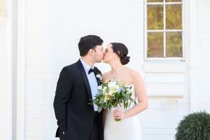 A romantic wedding couple shares a kiss outside a white mansion with elegant columns and windows at the foxglove in marietta, ga