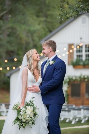 A romantic outdoor wedding scene with string lights and white chairs, featuring a couple embracing in formal attire. ivy and oak wedding
