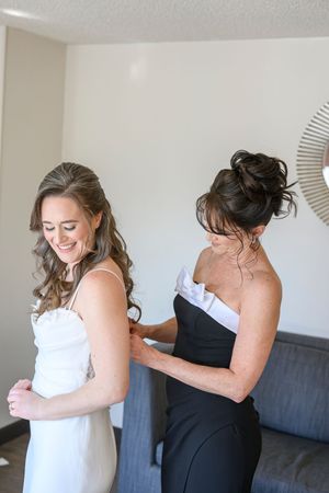 A bride in a white dress gets help with final adjustments while getting ready on her wedding day at flint hill in norcross, ga