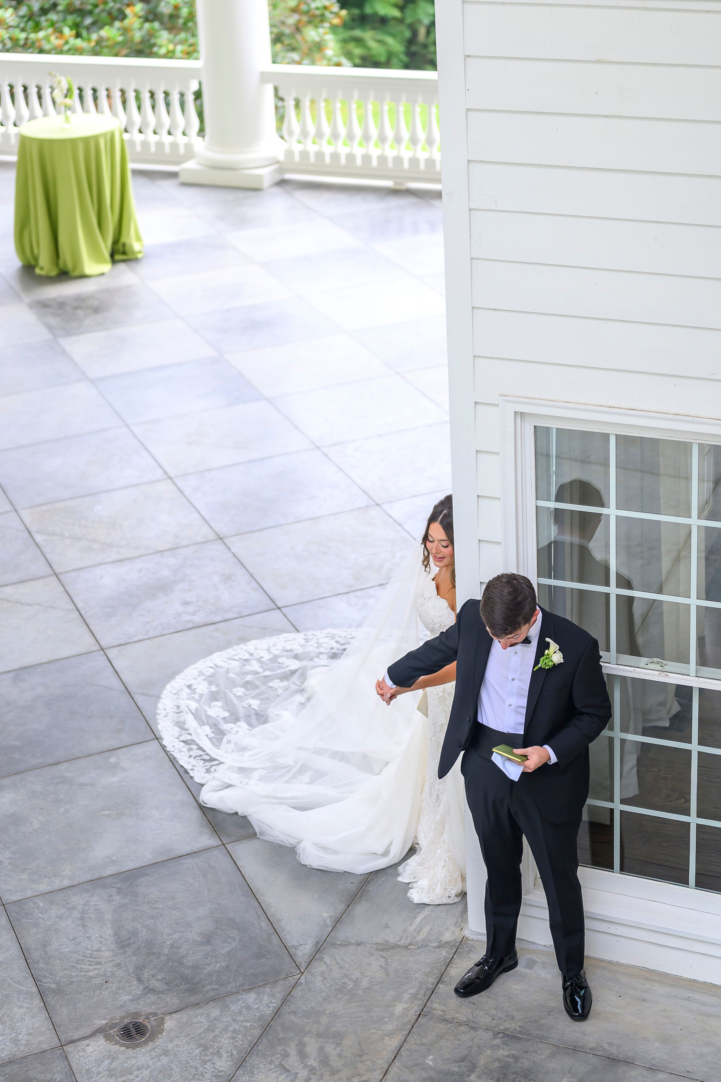 Aerial view of bride in white gown and groom in black tuxedo sharing a private moment on elegant venue patio. abbott mansion wedding photos