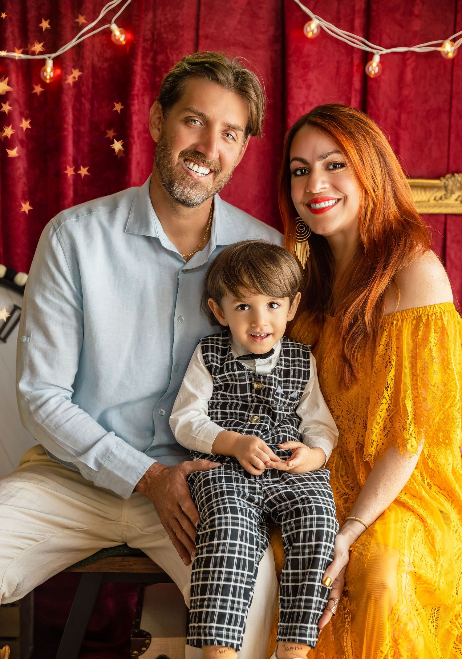 fotografia de mama papa y nino sentado en su falda mama esta vestida de amarilla mientras papa usa una camisa azul claro