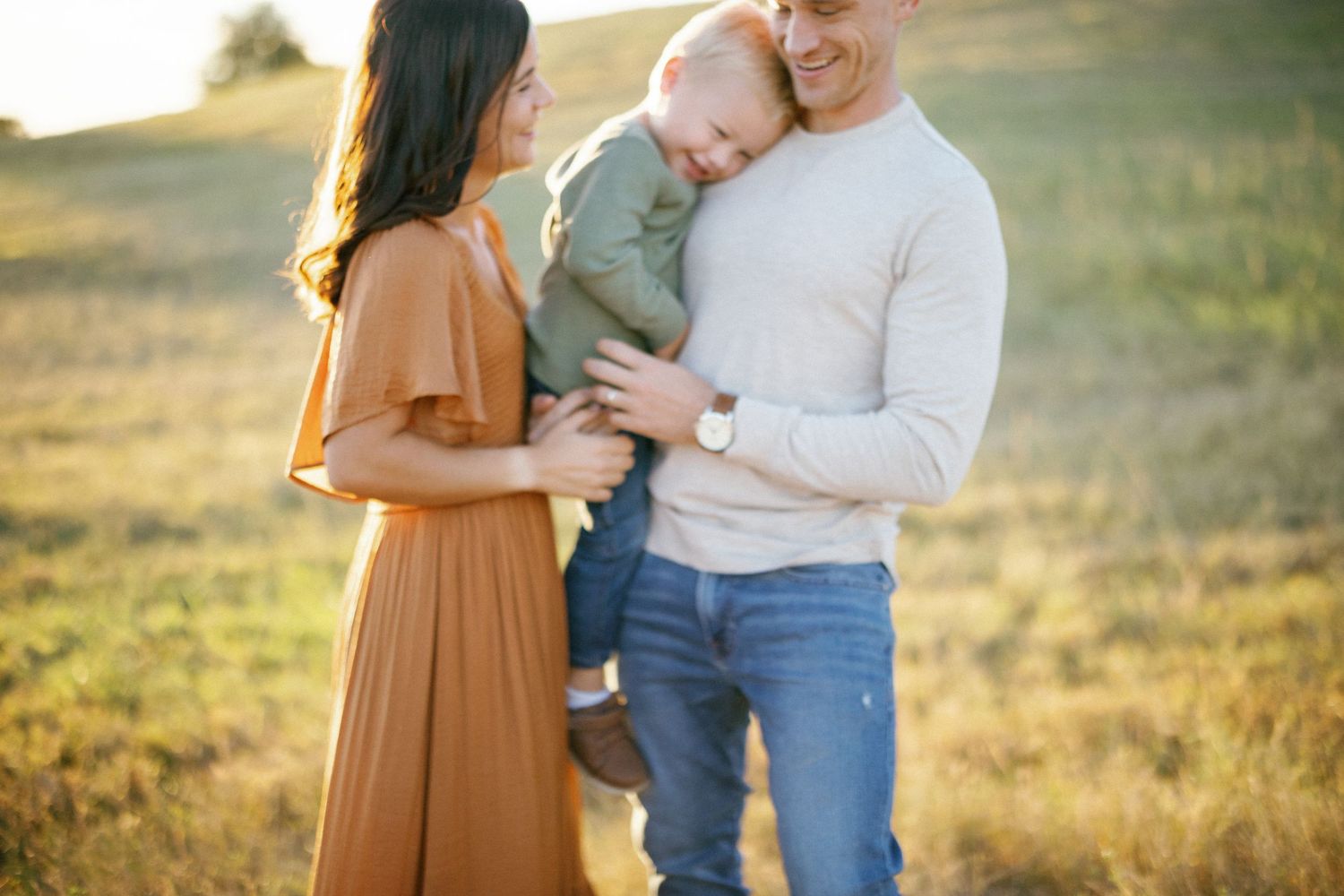 A family shares a tender moment together in a sunlit field during golden hour.