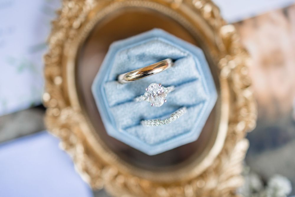 Elegant engagement ring displayed in ornate gold frames with soft blue velvet details and delicate floral accents.