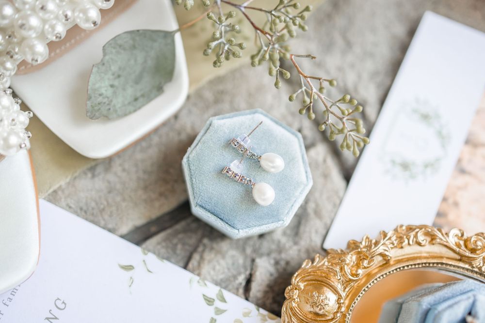 Wedding ring boxes and delicate pearl accessories arranged with baby's breath flowers on a textured surface.