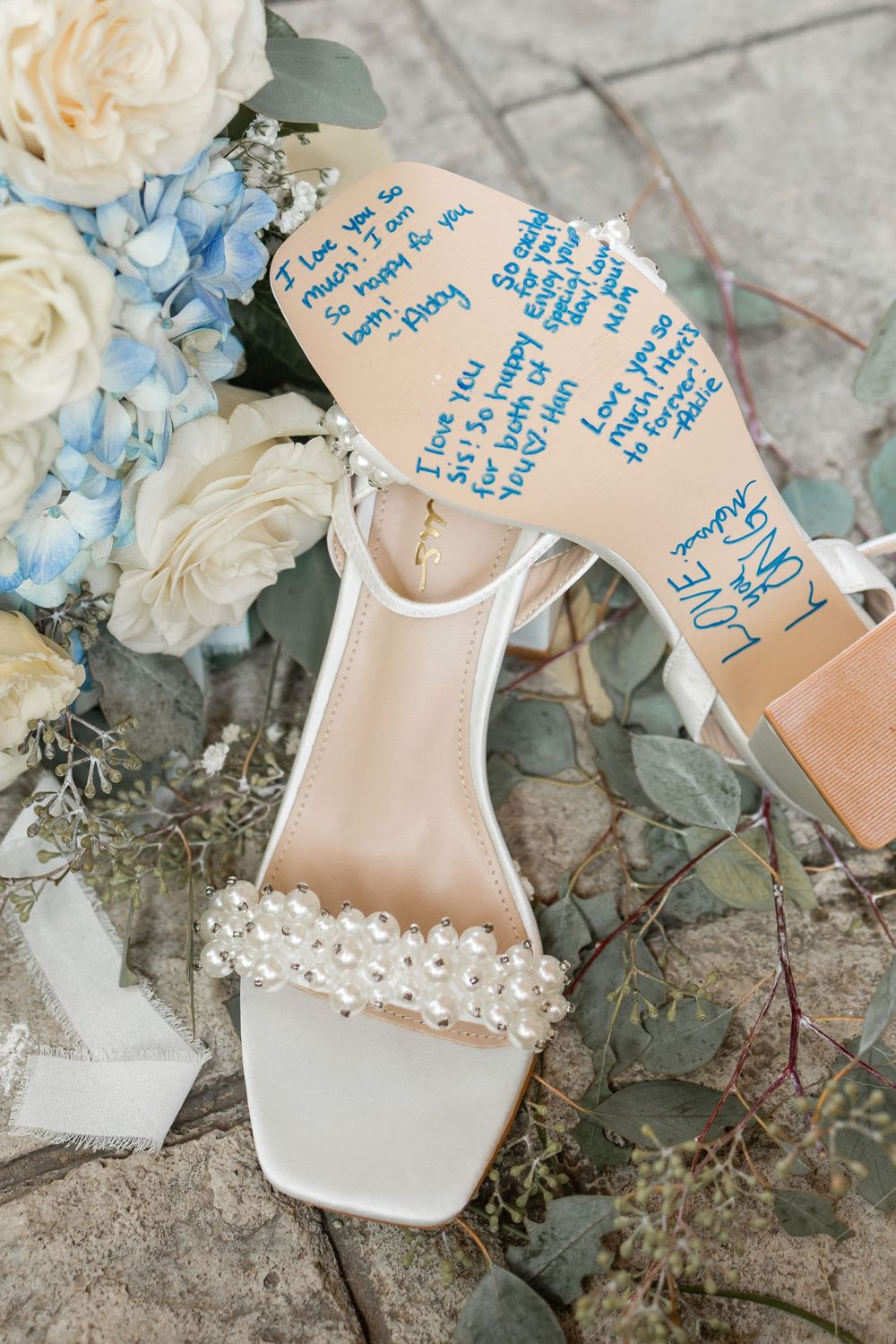 Elegant white wedding shoes with delicate pearl details displayed alongside blue hydrangeas and handwritten notes.