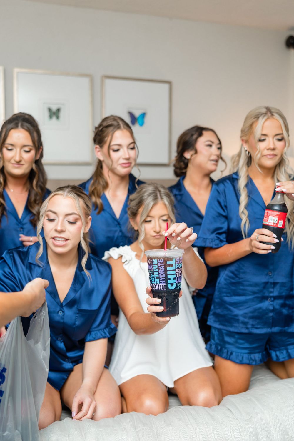 Bridesmaids in matching blue robes relax on a bed while drinking from cans in a fun photo series.