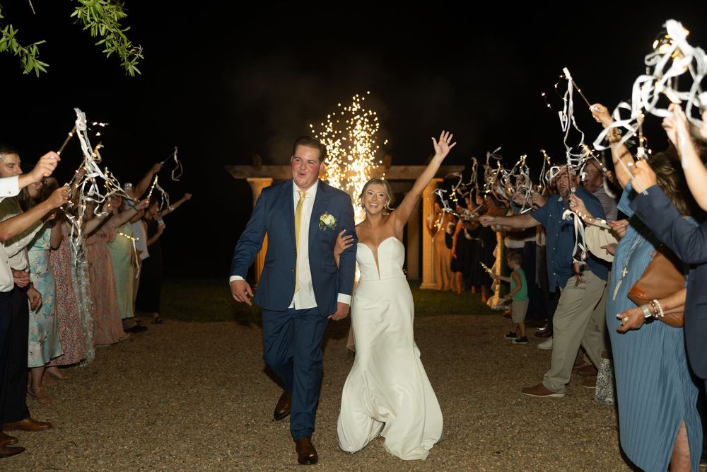 Wedding guests wave sparklers in celebration during an outdoor nighttime wedding send-off.