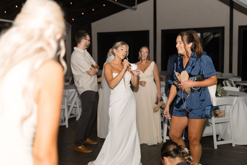 People dancing and celebrating at an indoor wedding reception with twinkling lights and white decor.