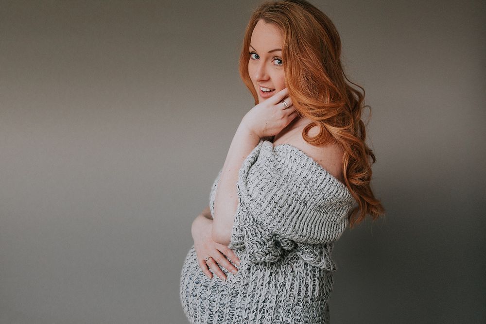 Woman in cozy gray sweater with long red hair poses against neutral background.