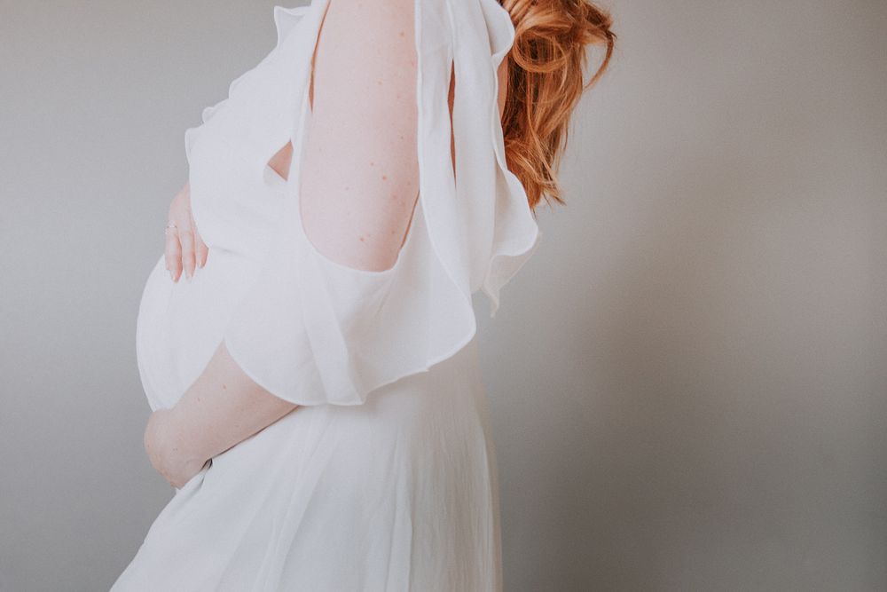A bride in a flowing white wedding dress stands elegantly against a soft gray background.