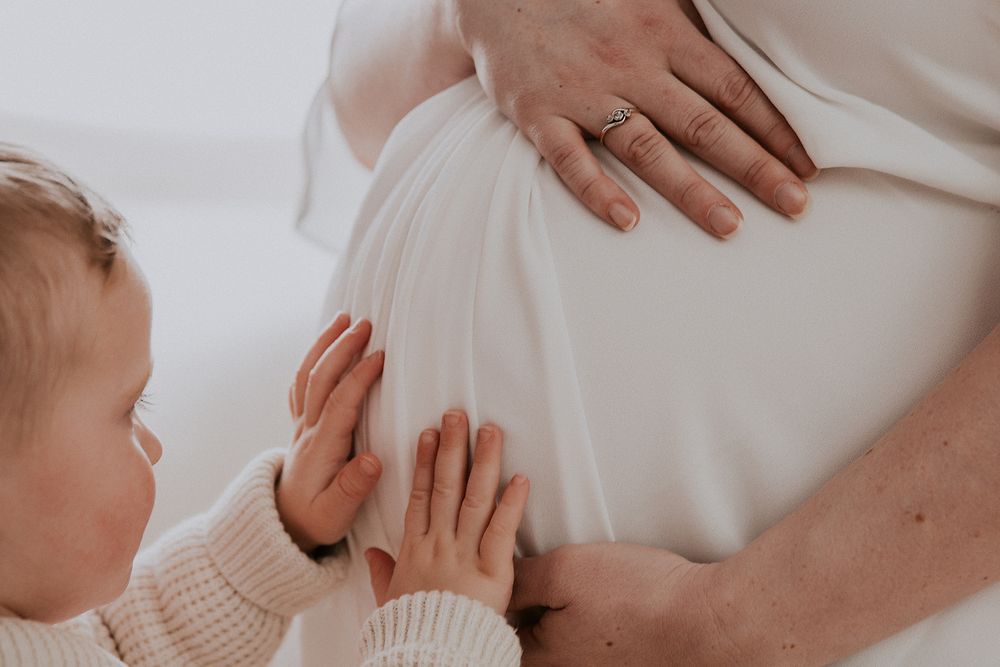 Small child's hands touching a pregnant belly while wearing a cream colored sweater.