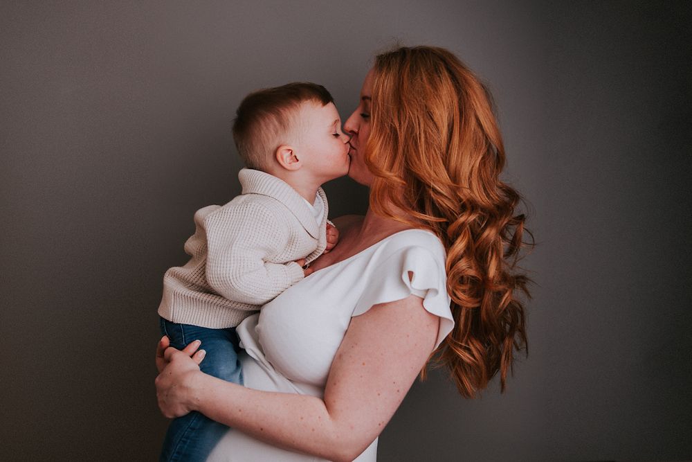 A tender moment between parent and baby in soft natural lighting against a dark background.