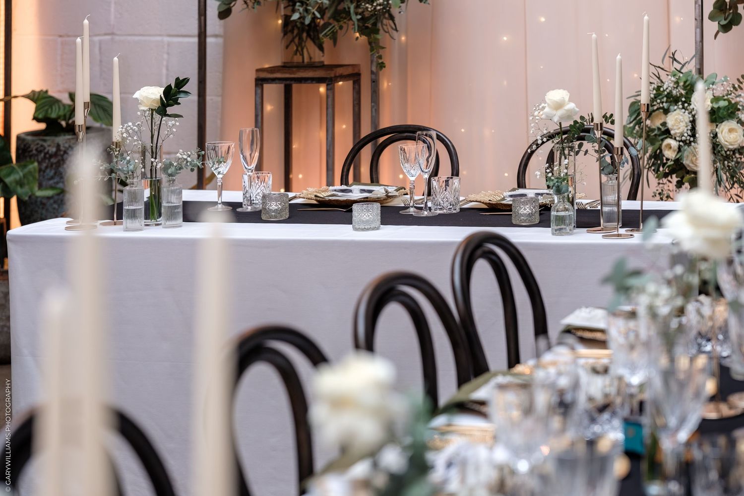 Elegant wedding reception table setup with black bentwood chairs and white floral arrangements in a modern venue.
