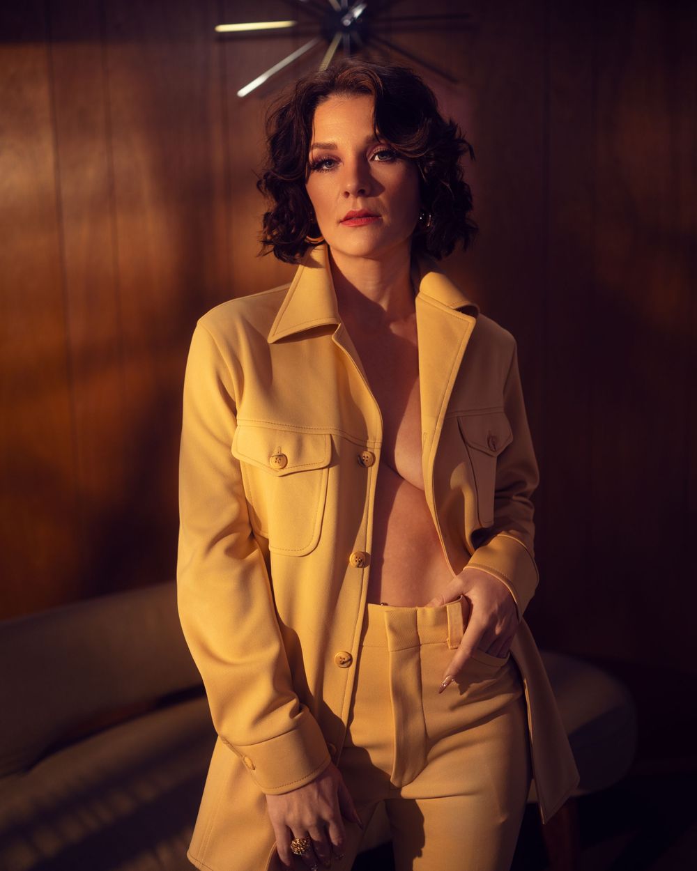 A figure in a cream-colored suit jacket poses dramatically against a warm-lit backdrop in a series of artistic portraits.
