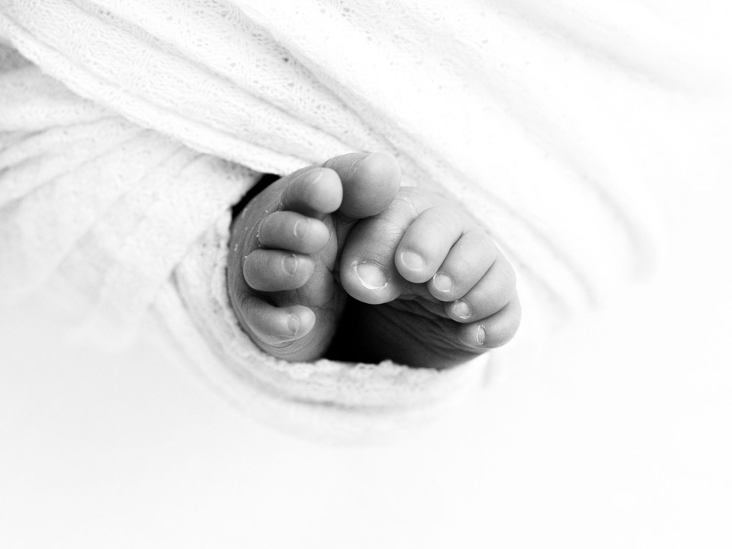 A sleeping baby with spiky black hair lies peacefully in soft white bedding.