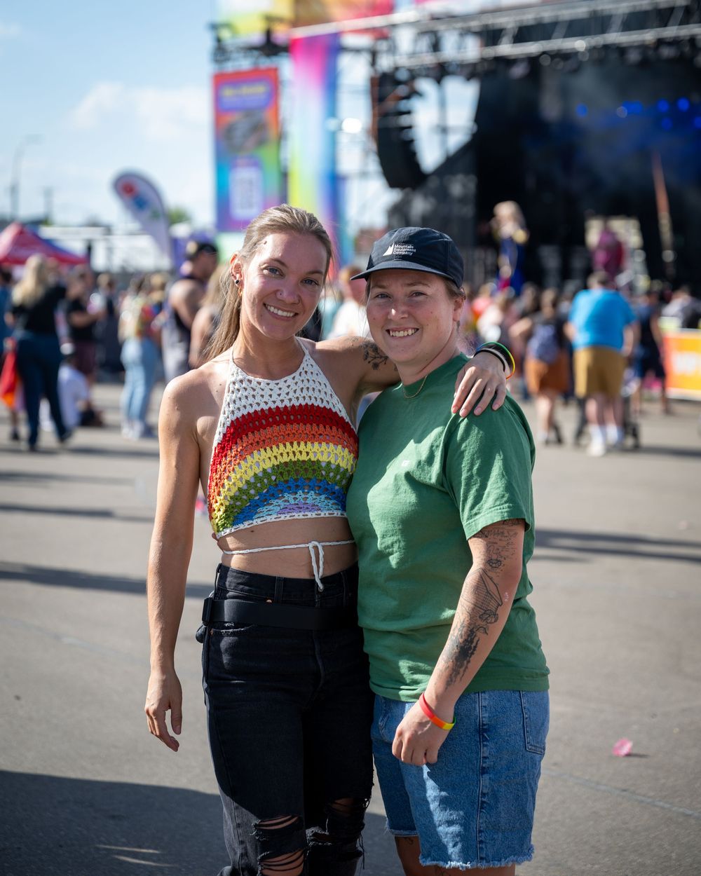 A couple in casual attire smiling and embracing at an outdoor festival or fairground.