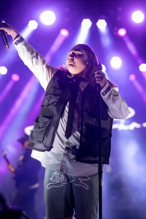 A performer sings passionately on stage with dramatic purple lighting and spotlights creating an atmospheric concert scene.