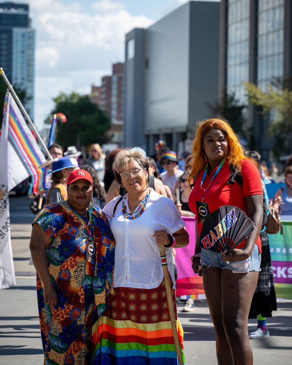 Diverse group of people celebrating at Pride festival with colorful flags and rainbow attire in an urban setting.
