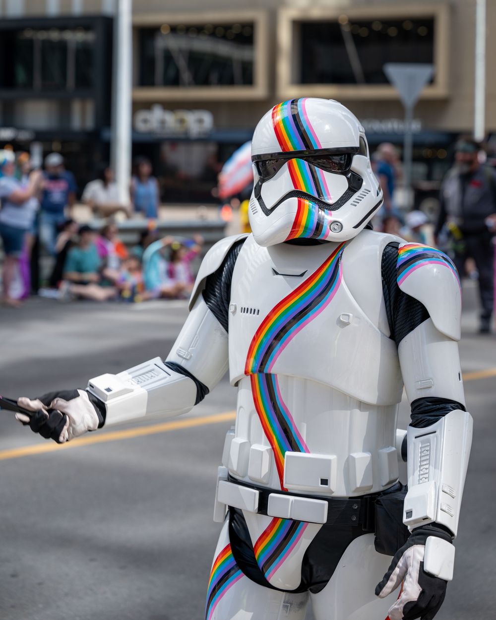 Stormtrooper costume with rainbow stripes marches in Pride parade along city street.