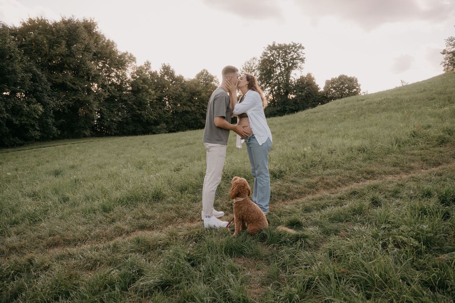 A couple shares a tender moment together on a grassy hillside during golden hour.