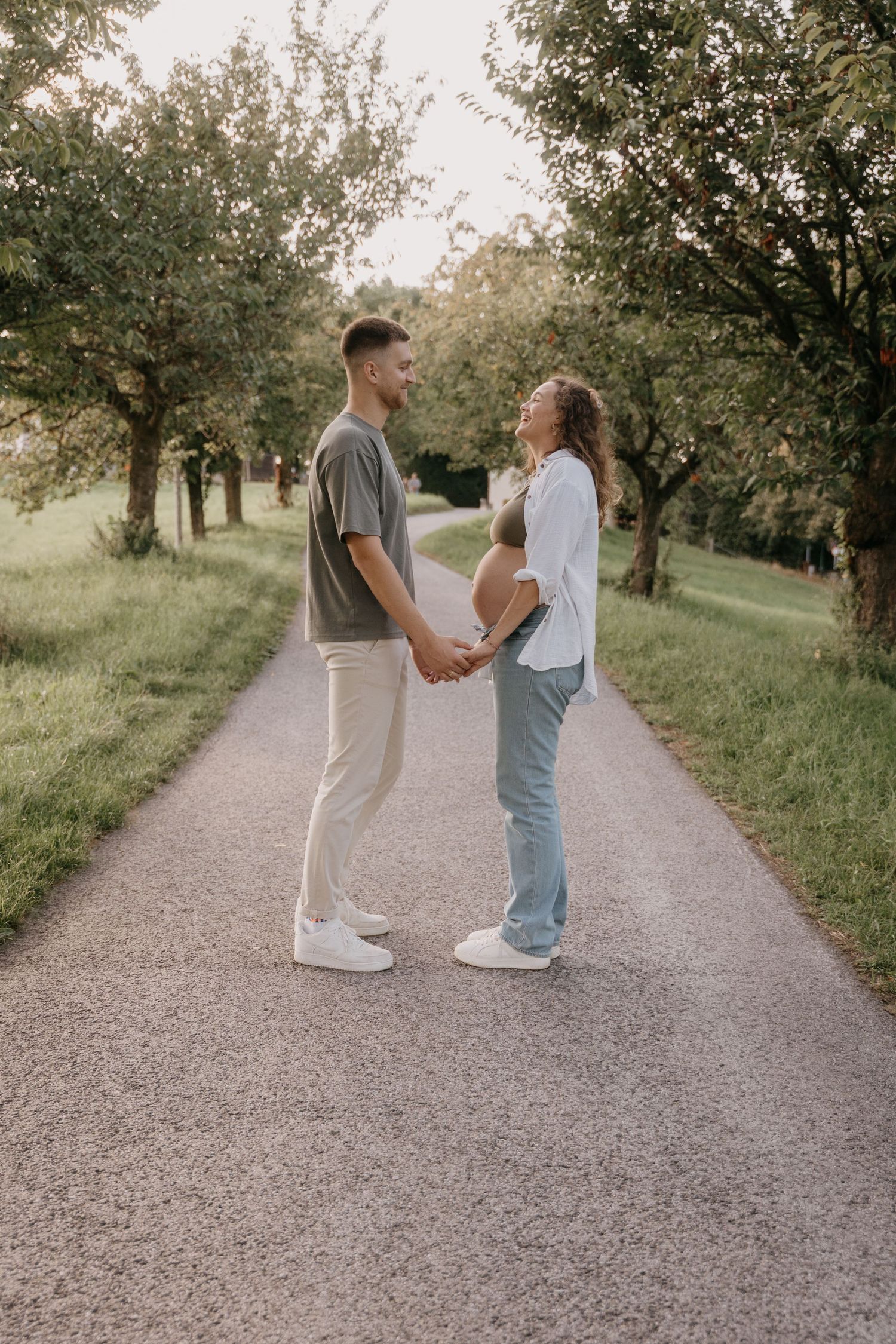 A couple walks hand in hand down a gravel path surrounded by blooming trees in a romantic outdoor setting.