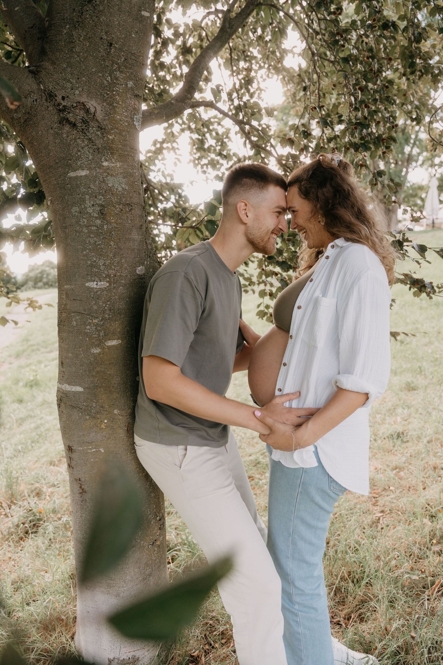 A romantic couple embraces tenderly under a sunlit tree canopy in a dreamy outdoor setting.