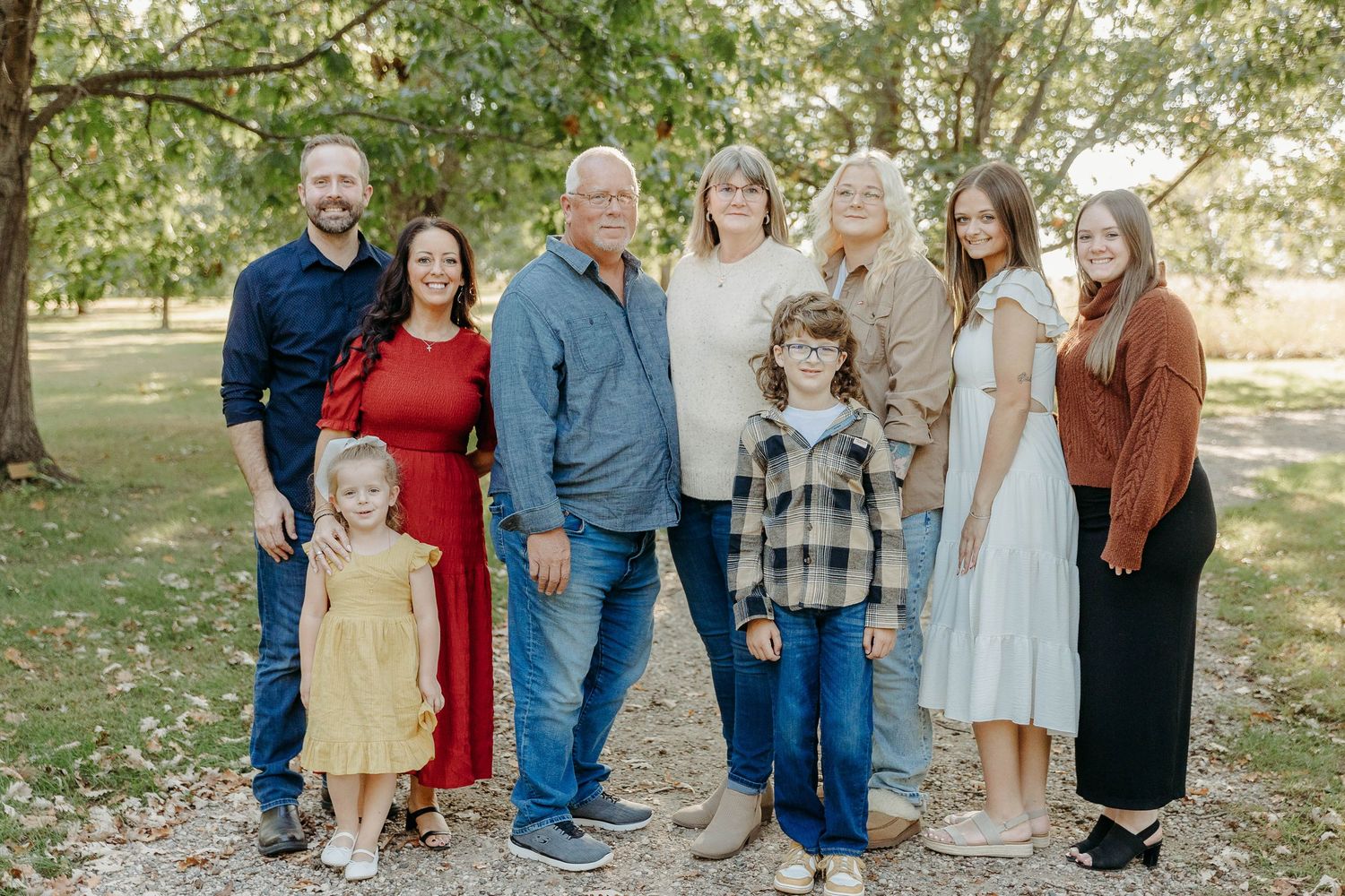 A multi-generational family poses together outdoors in coordinated casual outfits on a sunny autumn day.