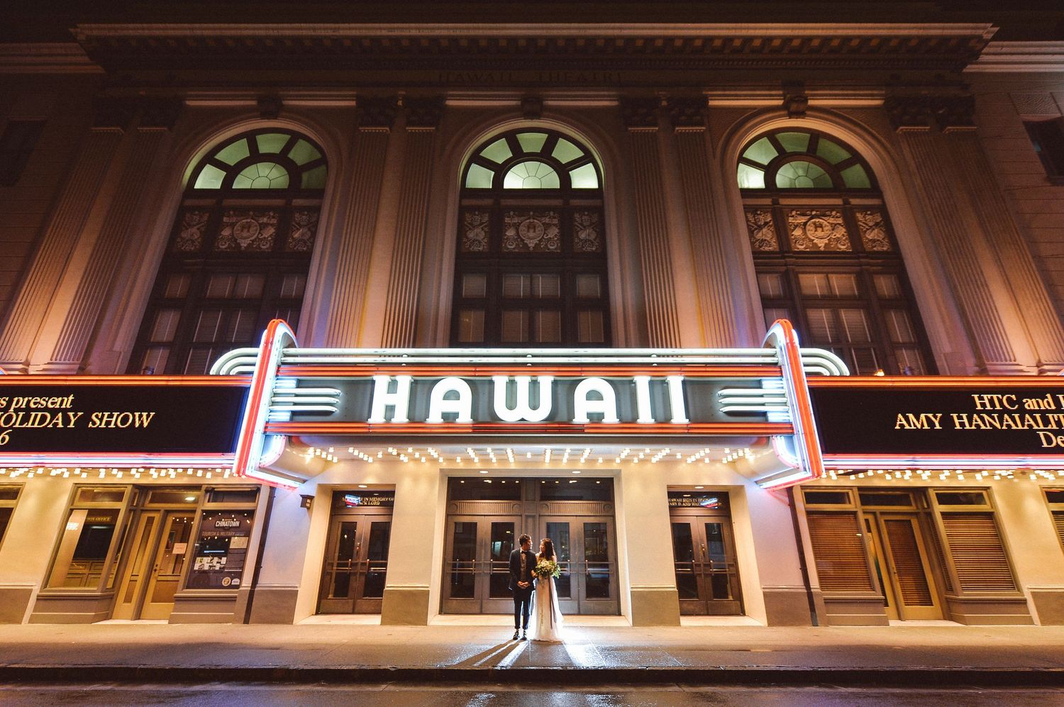 Couple poses at night in front of the illuminated Hawaii Theatre marquee in Honolulu, Hawaii.
ハワイシアター前フォト