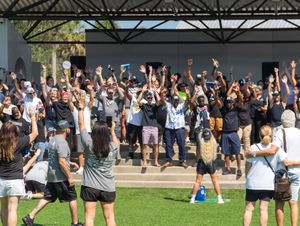 Large crowd of students celebrating outdoors on a sunny day with raised arms and excited expressions.