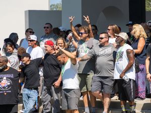 A large crowd of people outdoors wearing sunglasses and casual attire gesturing with peace signs and celebrating.