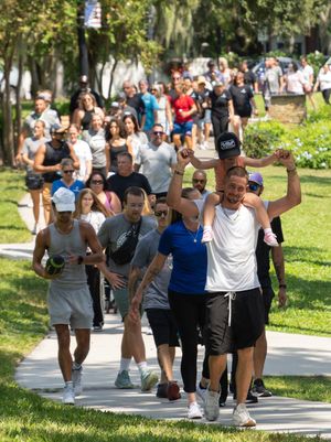 Large group of people exercising together on a tree-lined path in a sunny park during an outdoor fitness event.