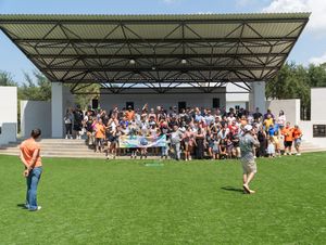 Large crowd gathered under a covered outdoor amphitheater structure during a daytime event.