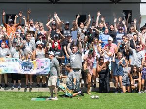 Large crowd of excited sports fans cheering and raising their arms at an outdoor stadium event.