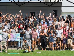Enthusiastic crowd cheers with raised arms at an outdoor venue during a sunny day.