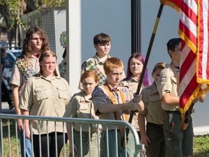 Boy scouts stand at attention during a flag ceremony with American flags raised outdoors.