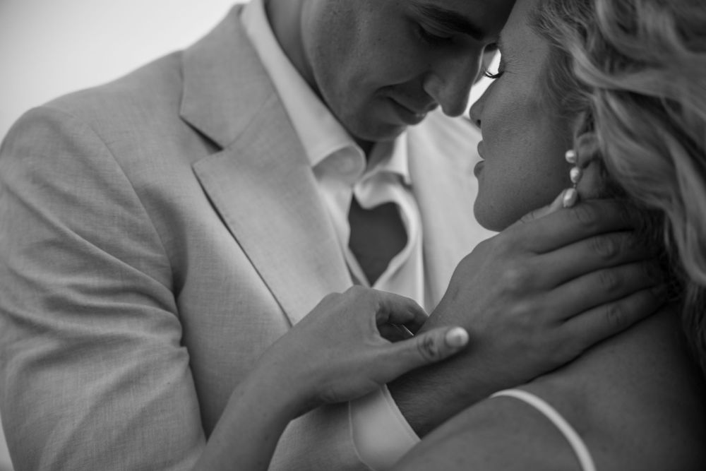 A romantic black and white close-up of a tender moment between a couple in formal wedding attire.