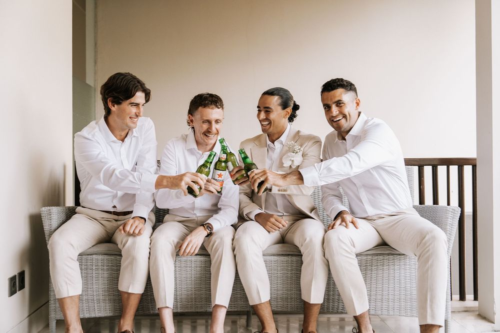 Four people in white shirts sit casually on a white railing while laughing and enjoying a lighthearted moment together.