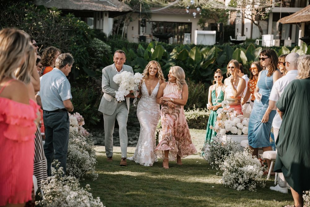 Wedding guests gather outdoors in floral dresses and light attire for a summer garden celebration.