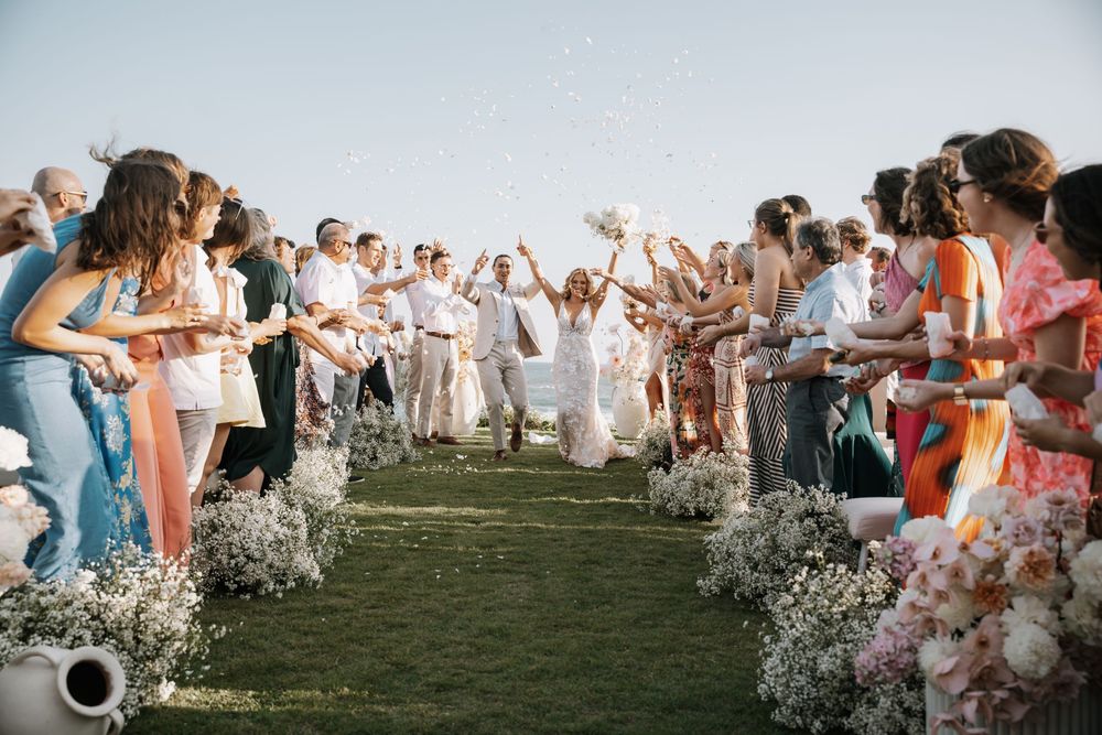 Wedding guests celebrate on a grassy lawn with baby's breath flower petals creating a magical atmosphere during sunset.