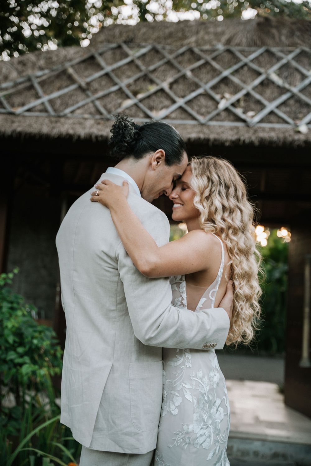 A romantic couple in wedding attire share an intimate moment under a latticed pergola during their wedding celebration.