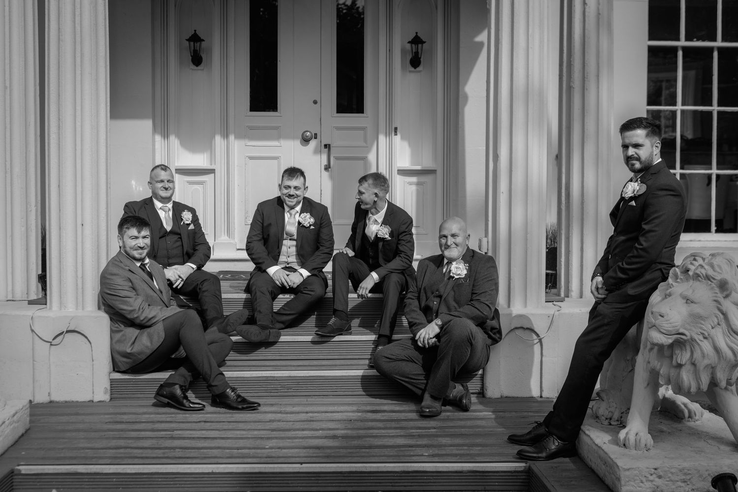 A black and white photo shows a group of people sitting along the steps of a building with white columns.