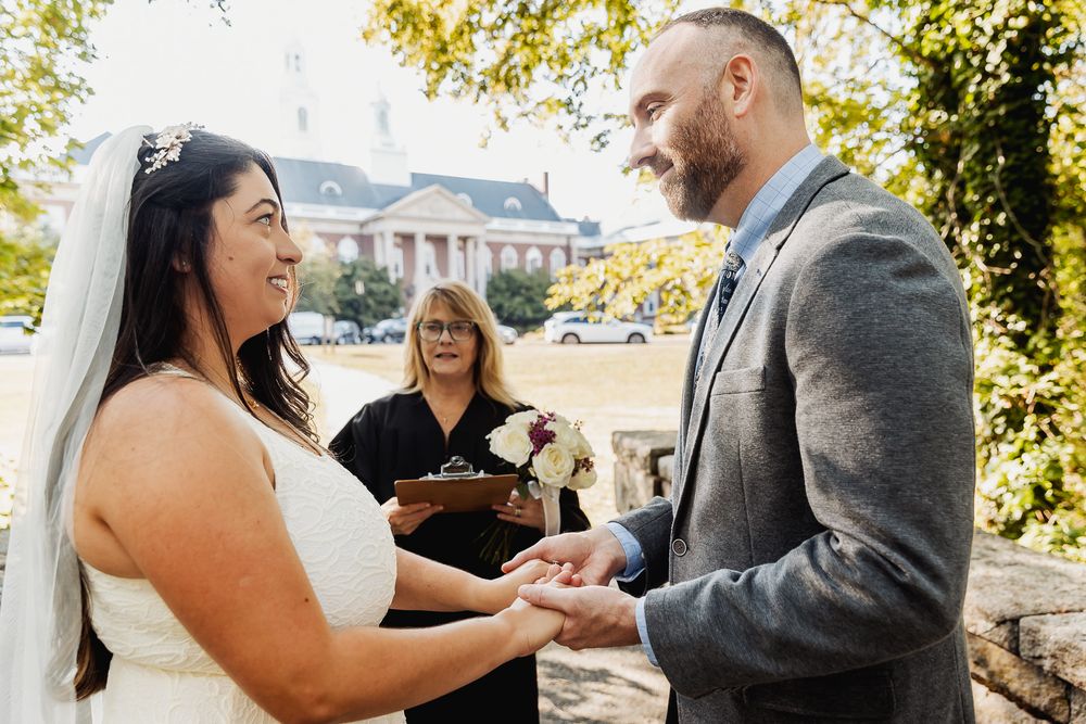 Couple sharing joyful moments during an outdoor wedding ceremony with autumn foliage in the background.