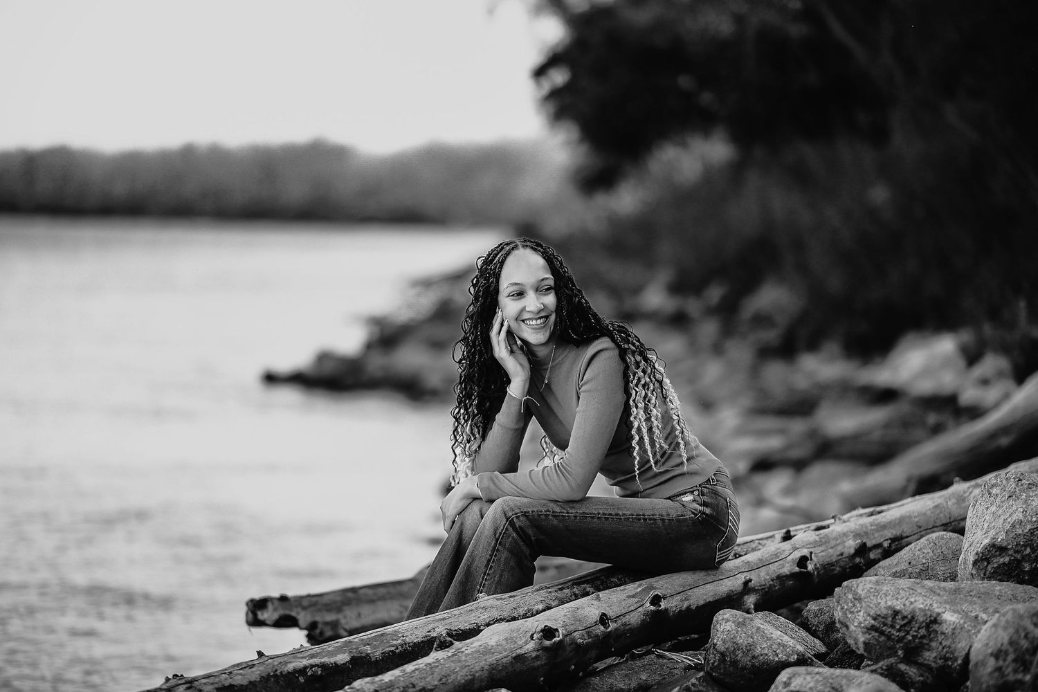 A black and white panoramic sequence of a person sitting on a fallen log by a serene lake or river.