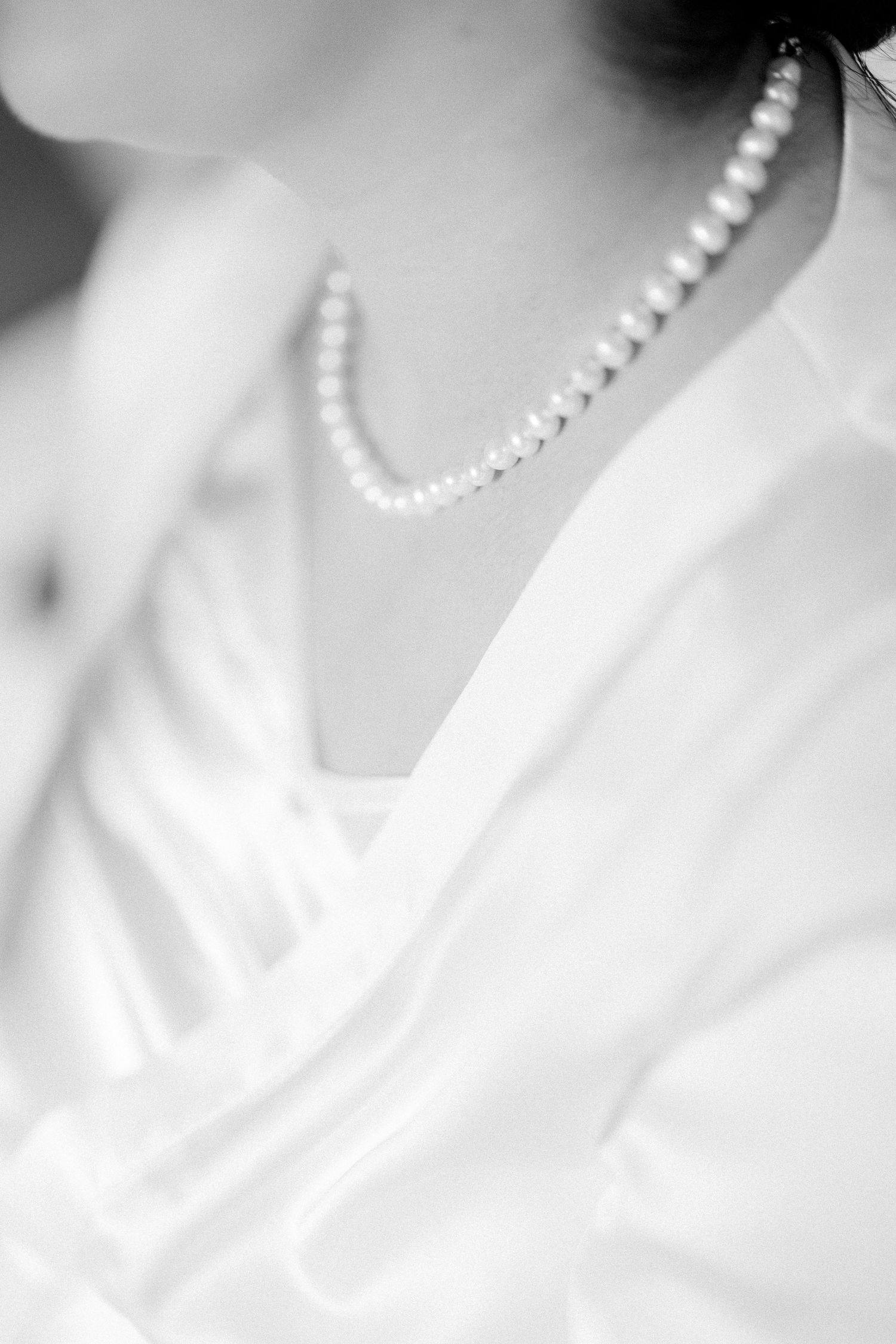 A delicate pearl necklace with round white beads creates an elegant curve against a soft white background.