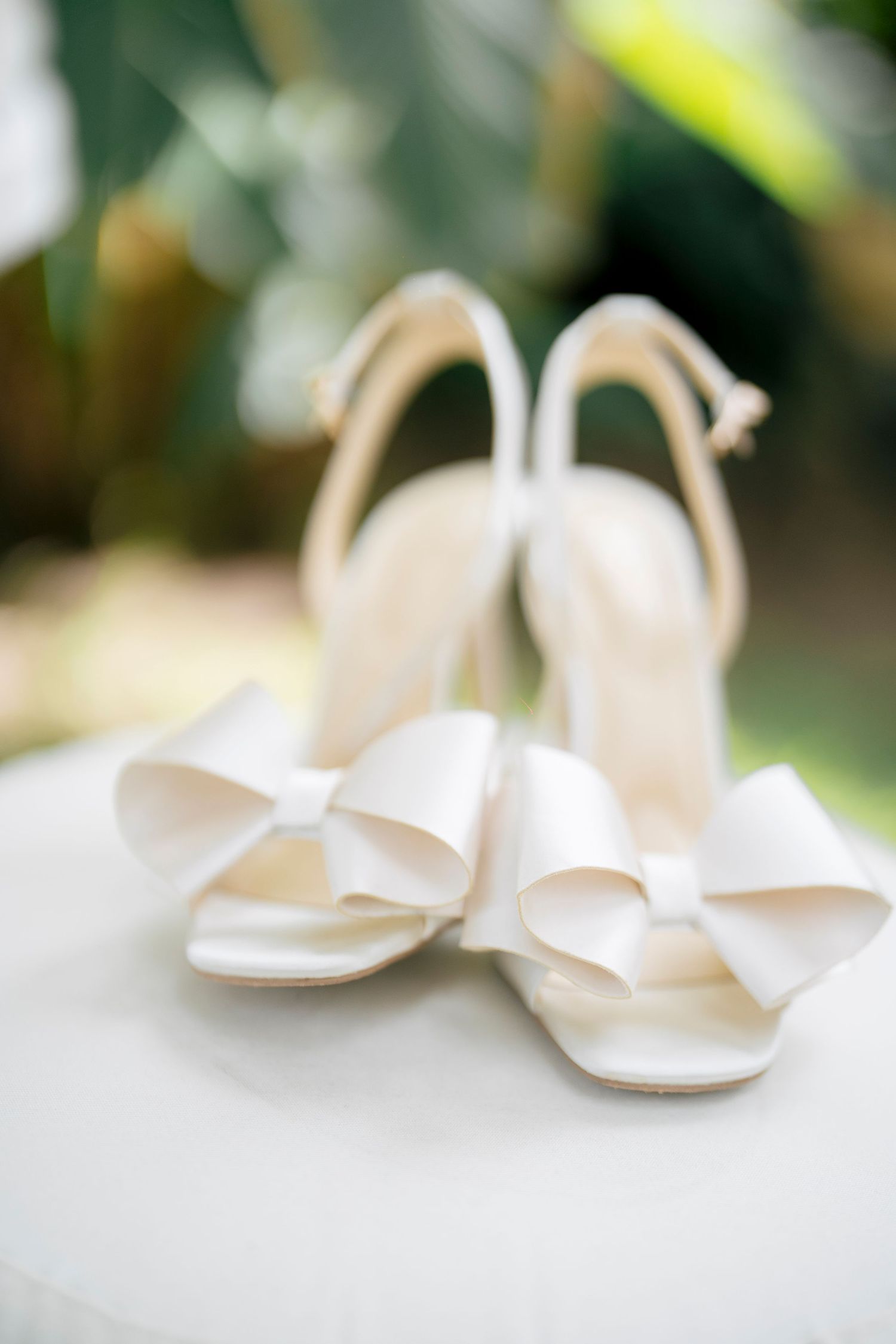 Elegant white bridal shoes with peep-toe design sit on a blurred natural background.