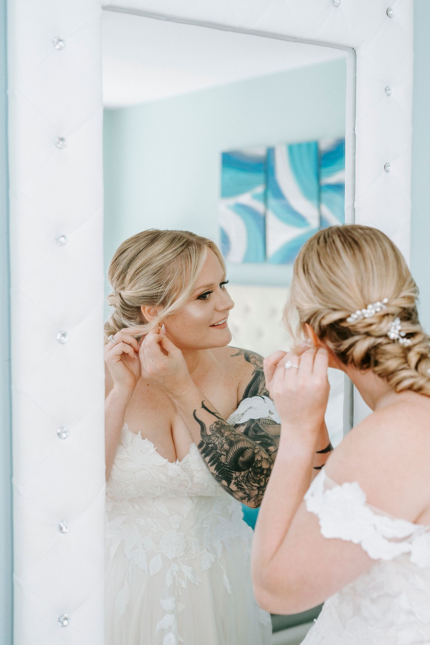 A bride getting ready in a bright white dressing room with mirrors reflecting her elegant wedding dress.