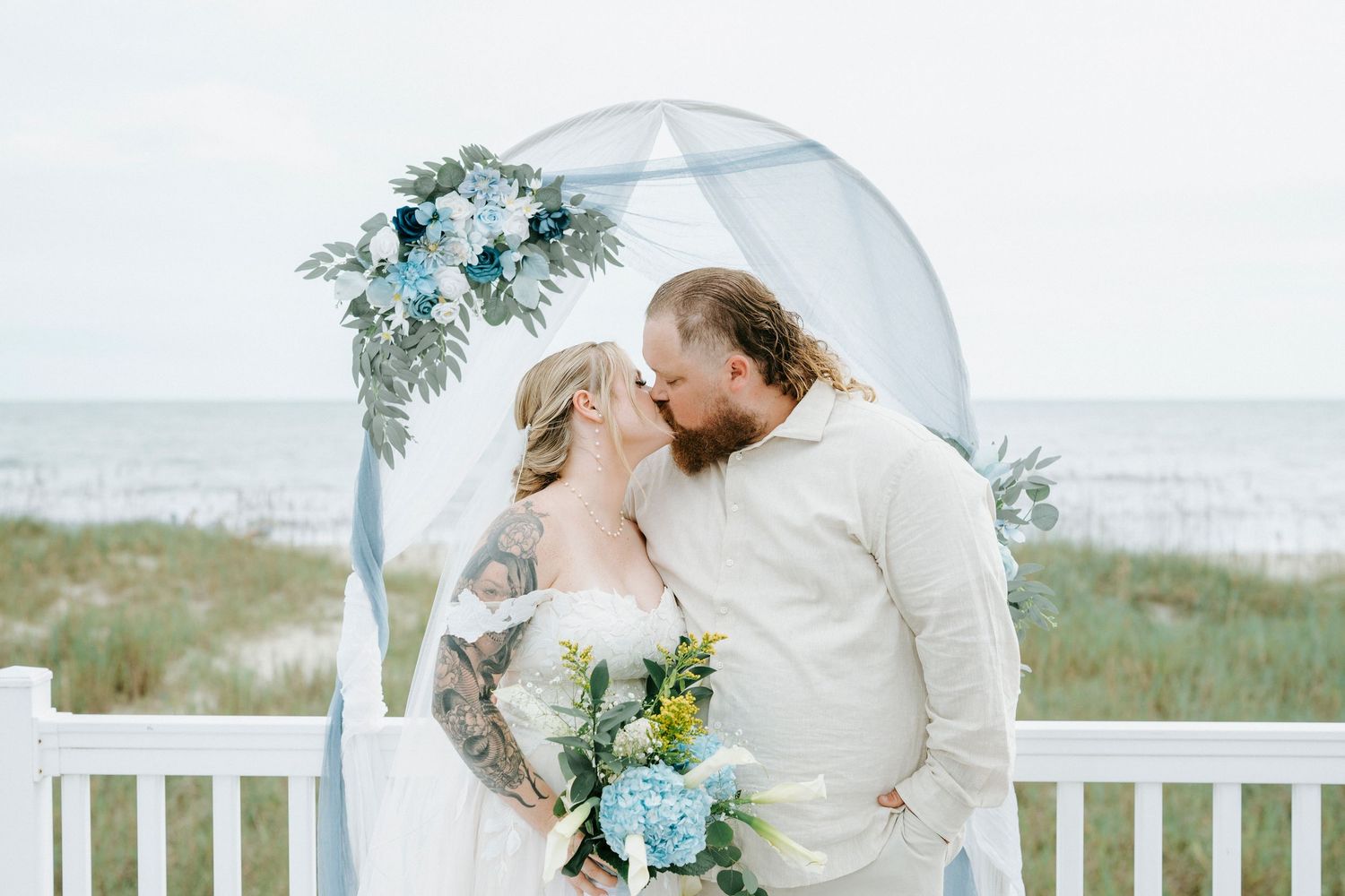 Newlyweds share an intimate moment on a white bench overlooking the ocean.