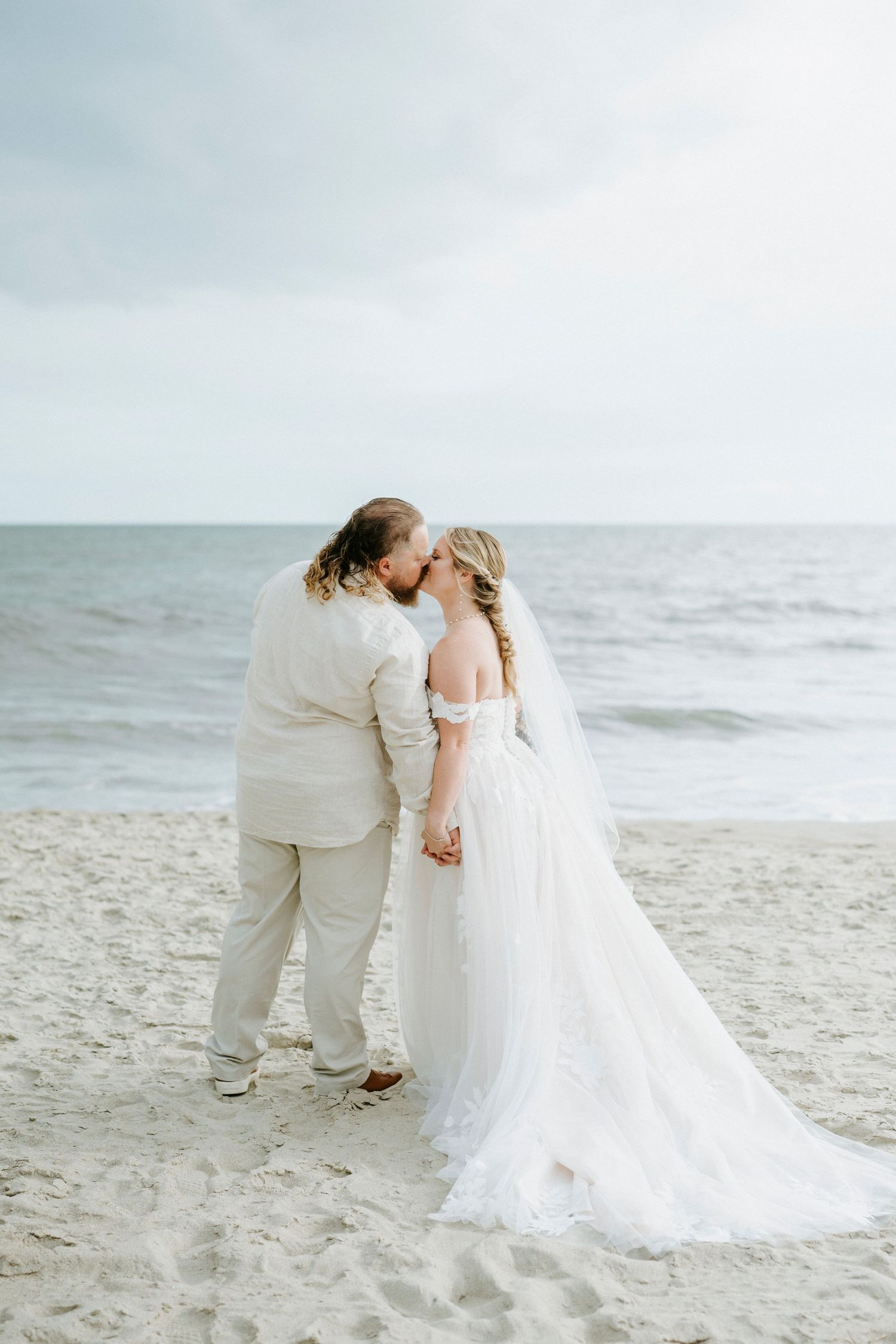 A romantic beach wedding photo series showing a couple in white attire embracing on the sandy shoreline.